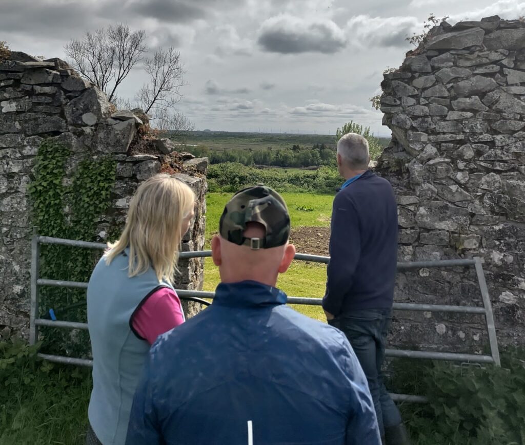 three people look out at a bog through an old stone wall in offaly